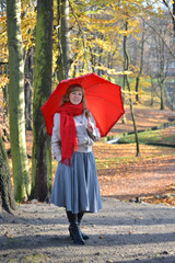 The happy young woman costs with a red umbrella in the autumn pa