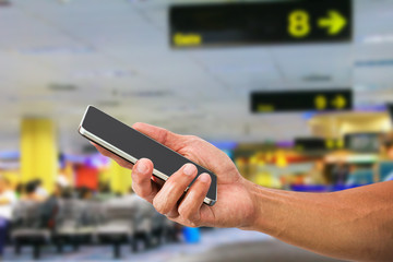 Man's hand holding mobile phone on blured departure hall in airport