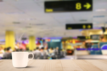 Hot white coffee cup on wooden table on blurred departure hall in airport