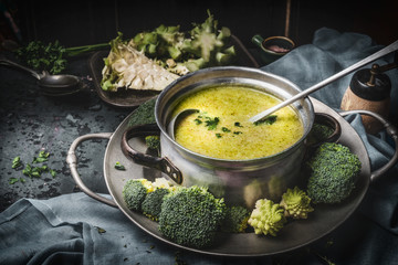 Cooking pot with green romanesco and broccoli soup and ladle on dark rustic kitchen table . Healthy...