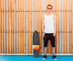 Urban man sunglasses and skateboard posing on wood planks background. Good looking. Cool guy. Wearing white shirt and black pants.