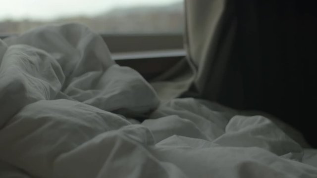 Morning scene with rumpled blanket and city view in the window near bed
