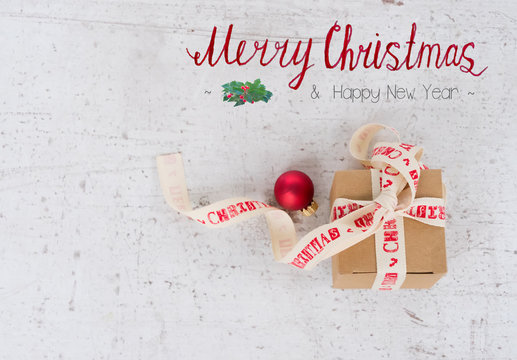 Christmas flat lay styled scene - present box with red ball on wooden white table with merry christmas greetings