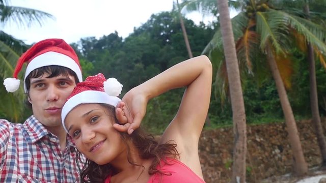 Happy joyful couple on Christmas travel holidays taking selfie picture with smartphone wearing santa hat during sunset in slow motion. 1920x1080