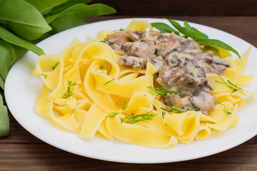 Fettuccine pasta in a creamy sauce with mushrooms on  plate   wooden table. Horizontal top view. Close-up
