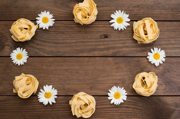 Raw fettuccine with flowers on wooden background. Italian Cuisine. Top view. Close-up