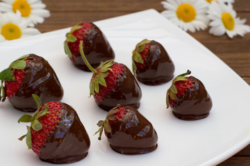 Strawberries dipped in chocolate on a white square plate. Wooden background. Close-up