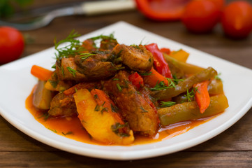 Stew with potatoes, carrots, pickles, tomatoes and hot peppers. Azu by Tartarian on a white square plate. Wooden rustic background. Top view. Close-up