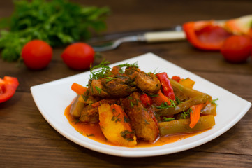 Stew with potatoes, carrots, pickles, tomatoes and hot peppers. Azu by Tartarian on a white square plate. Wooden rustic background. Top view. Close-up
