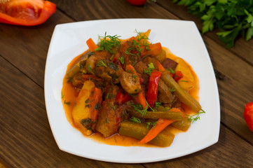 Stew with potatoes, carrots, pickles, tomatoes and hot peppers. Azu by Tartarian on a white square plate. Wooden rustic background. Top view. Close-up