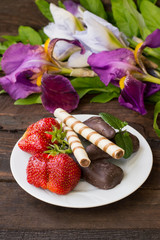 Strawberries with chocolate on a background of flowers. Wooden table. Close-up