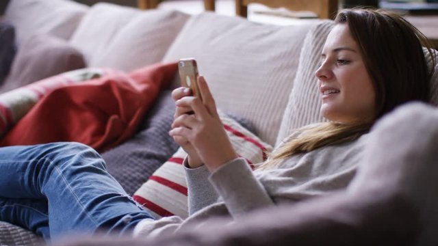 4K Attractive young woman relaxing at home on her couch using her cell phone, in slow motion