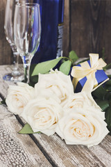 White roses, sparkling wine bottle, champagne glasses on a woode