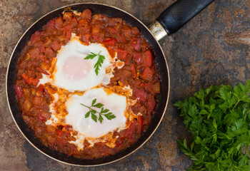 Shakshuka in a frying pan. Traditional Jewish dish. Wooden table. Top view. Close-up
