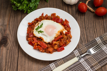 Shakshuka on a white plate. Traditional Jewish dish. Wooden table. Close-up