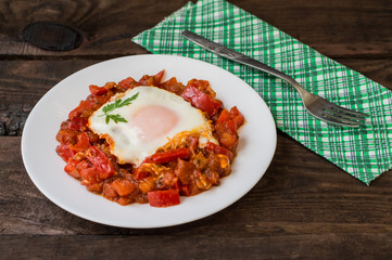 Shakshuka on a white plate. Traditional Jewish dish. Wooden table. Close-up