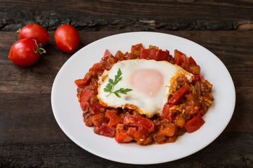 Shakshuka on a white plate. Traditional Jewish dish. Wooden table. Close-up