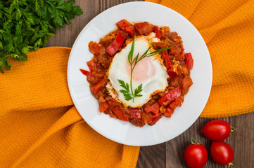 Shakshuka on a white plate. Traditional Jewish dish. Wooden table. Top view. Close-up