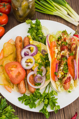 Ingredients for a picnic consisting of vegetables and sausages grilled on wooden rustic background, top view. Close-up