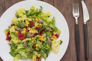 Salad from beef tongue, Chinese cabbage, peppers, corn, parsley and basil. Wooden background. Top view