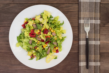 Salad from beef tongue, Chinese cabbage, peppers, corn, parsley and basil. Wooden background. Top view