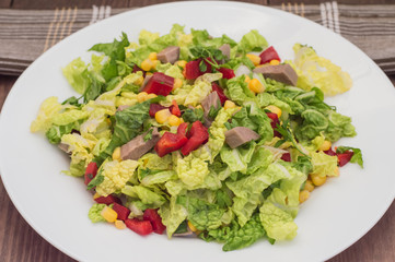 Salad from beef tongue, Chinese cabbage, peppers, corn, parsley and basil. Wooden background. Top view