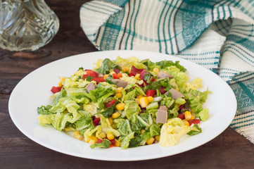 Salad from beef tongue, Chinese cabbage, peppers, corn, parsley and basil. Wooden background. Top view