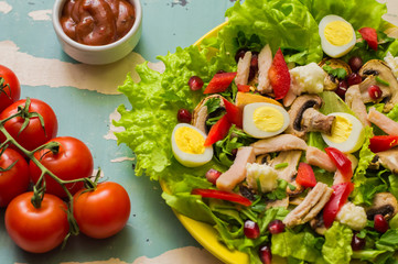 Salad with mushrooms, chicken, quail eggs, paprika, lettuce and pomegranate, on a old table. Top view
