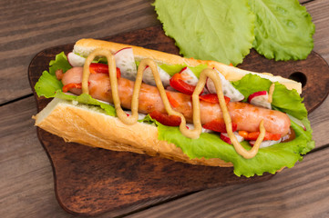 Hot dog with grilevskoy sausage, lettuce, radish and mustard, on a wooden background. Top view