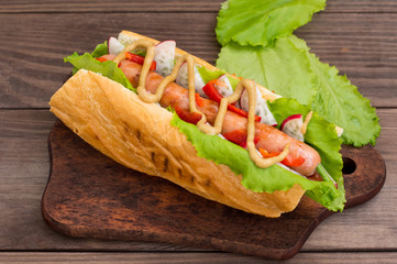 Hot dog with grilevskoy sausage, lettuce, radish and mustard, on a wooden background. Top view