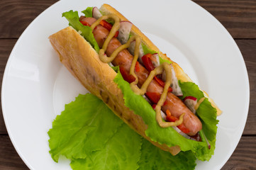 Hot dog with grilevskoy sausage, lettuce, radish and mustard, on a wooden background. Top view