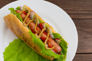 Hot dog with grilevskoy sausage, lettuce, radish and mustard, on a wooden background. Top view
