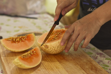 Close up woman’s hands cutting fresh melon with knife and wooden chopping board