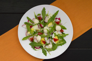 Salad with radishes, arugula, chicken and quail egg on a wooden background, top view