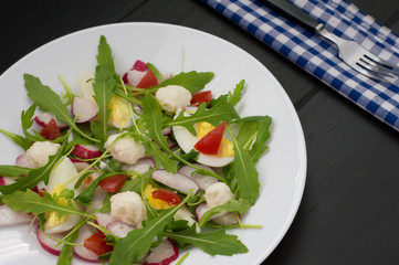 Salad with radishes, arugula, chicken and quail egg on a wooden background, top view