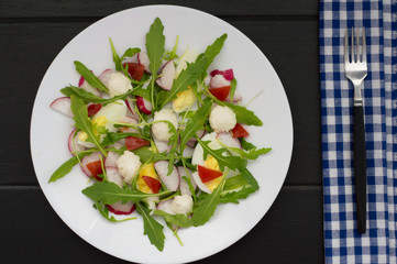 Salad with radishes, arugula, chicken and quail egg on a wooden background, top view