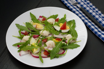 Salad with radishes, arugula, chicken and quail egg on a wooden background, top view