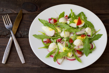 Salad with radishes, arugula, chicken and quail egg on a wooden background, top view