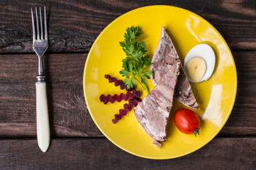 Headcheese on a yellow plate. Wooden background. Top view