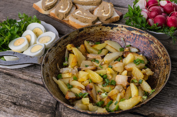 Fried potatoes in lard with herbs on an old wooden table. Top view. Close-up