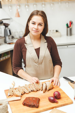 Young woman is preparing some food in the kitchen. She cutting a bread