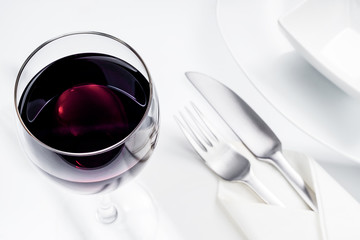 Rotwein im Glas mit Geschirr und Servette auf weißem Tisch, Draufsicht