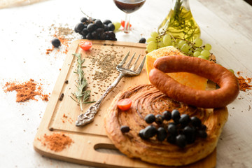 sausage,cheese,bread,grapes,a glass of red wine on wooden Board