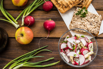Salad with radishes, apples, greens and a sandwich  fish pate. Wooden background. Top view. Close-up