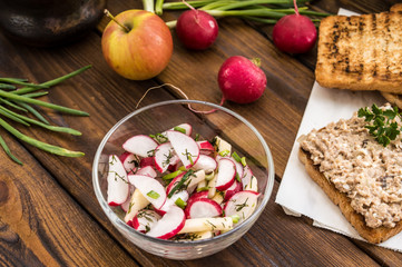 Salad with radishes, apples, greens and a sandwich  fish pate. Wooden background. Top view. Close-up