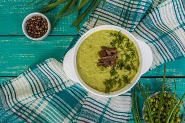 Puree soup with peas, melted cheese, roasted meat, croutons and herbs. Wooden background. Top view. Close-up