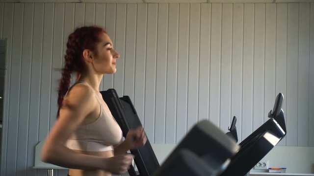 Attractive caucasian girl running on the treadmill in the sport gym.