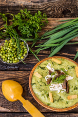 Puree soup with peas, melted cheese, roasted meat, croutons and herbs. Wooden background. Top view. Close-up
