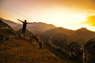 Man on the top of hill watching wonderful landscape of mountains in the rays of sunset