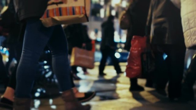 Christmas holiday shoppers at night, cross busy city street,slow motion 100p.Anonymous crowd of pedestrians cross a busy city street on a December night carrying shopping bags.No logos/faces visible